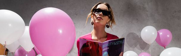 Tiefansicht einer stilvollen Frau mit Sonnenbrille, die ein Magazin in der Nähe von Luftballons hält, Banner  - Foto, Bild