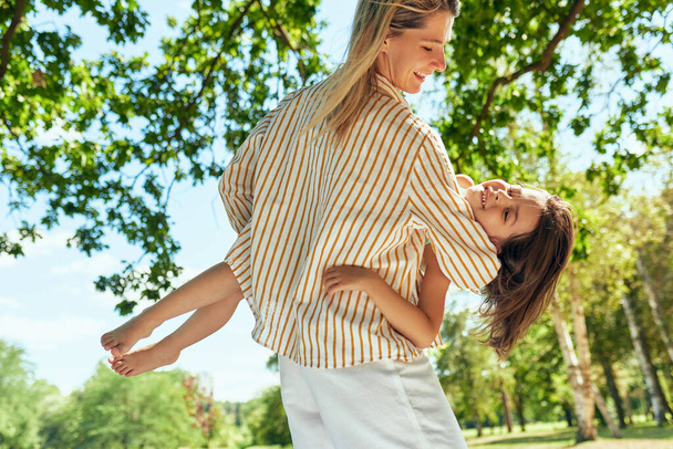 Horizontal image of happy mother and her joyful little girl playing in the park during the picnic. Happy woman and daughter smiling and spending time together on a sunny day. Mother's day concept. - Foto, imagen
