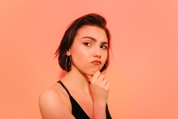 thoughtful young woman looking away with hand near face on orange background - Photo, Image
