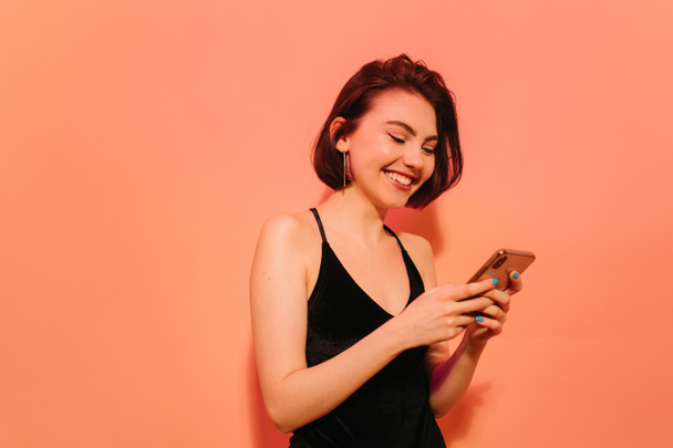 happy young woman with cellphone in hands on orange background - Фото, изображение