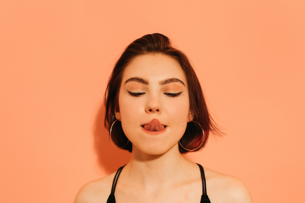 young woman grimacing with sticking out tongue on orange background - Photo, Image