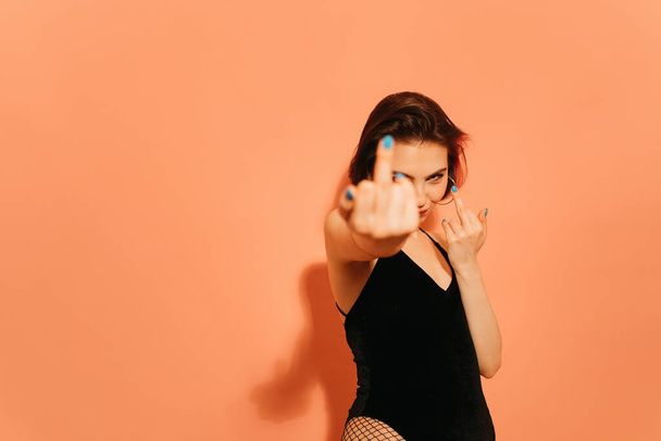 young woman with provocative middle fingers gesture on orange background - Фото, изображение