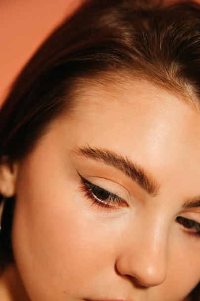 close up of young woman cropped face with shiny summer cat eyes makeup isolated on orange - Fotografie, Obrázek