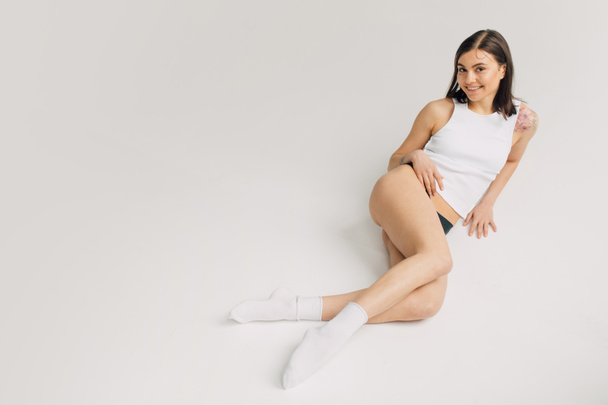 relaxed young woman in white top, socks and black panties lying on grey background - Фото, зображення