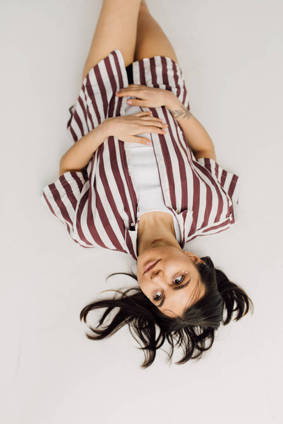 top view of dreamy young woman in striped shirt lying on grey background - Photo, Image