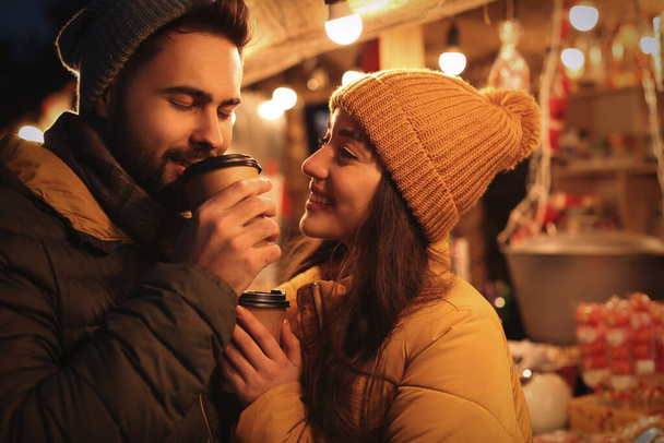 Lovely couple with cups of hot drinks spending time together at Christmas fair - Foto, imagen