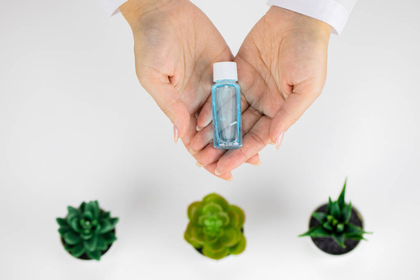 Botella cosmética con líquido en las manos sobre fondo blanco con plantas, espacio para copiar - Foto, imagen