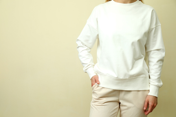 Junge Frau im weißen Sweatshirt vor beigem Hintergrund - Foto, Bild