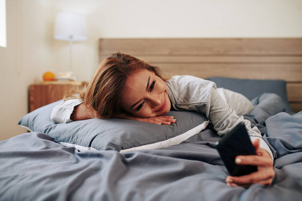 Usmívající se a pláč krásná mladá žena ležící na posteli a video volá její frind nebo člen rodiny - Fotografie, Obrázek
