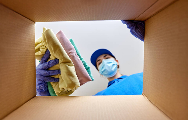 woman in mask packing clothes to parcel box - Foto, Bild