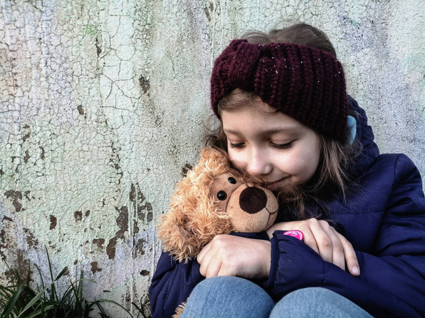 little teenager girl with favorite toy teddy bear on old grunge wall background - Photo, Image