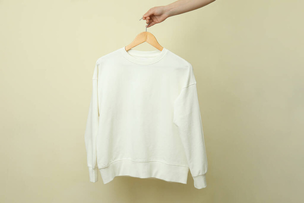 Hanger with white sweatshirt against beige background - Fotó, kép