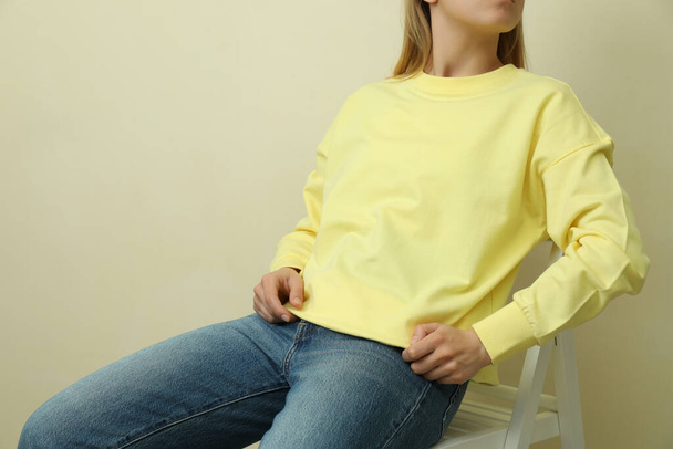 Giovane donna in felpa gialla seduta sullo sfondo beige - Foto, immagini