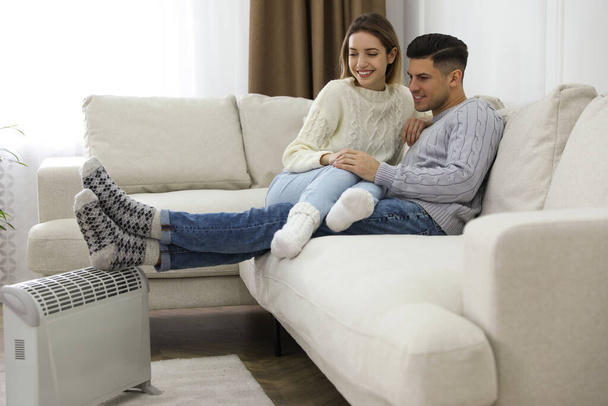 Szczęśliwa para siedzi na kanapie w pobliżu grzałki elektrycznej w domu - Zdjęcie, obraz