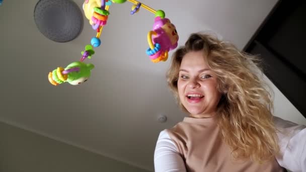Fröhliche Frau mit lockigem Haar spricht gebeugt über Wiege - Filmmaterial, Video