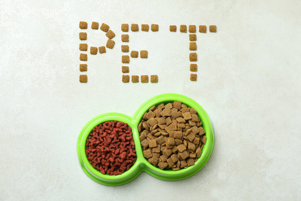 Palabra mascota hecha de pienso y cuencos de alimentación sobre fondo texturizado blanco - Foto, imagen