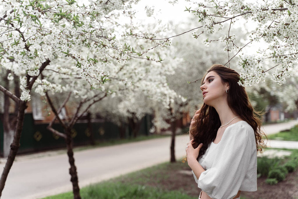 Estilo de vida. Modelo posando cerca de árboles blancos en flor sin máscara de campo al aire libre. Chica soñadora con el pelo rizado - Foto, imagen