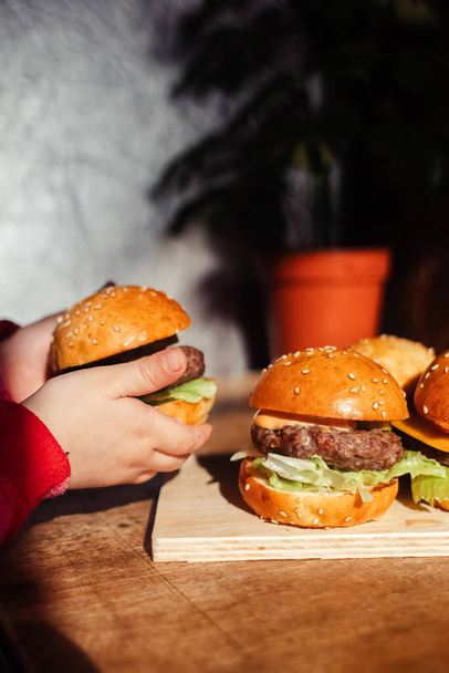 Mini-Burger auf einem Stand in Großaufnahme. Fast Food für Kinder in einem Restaurant oder Café. Makrofoto von Burger-Zutaten mit Fleisch und Gemüse. Öko-Burger für Kinder - Foto, Bild
