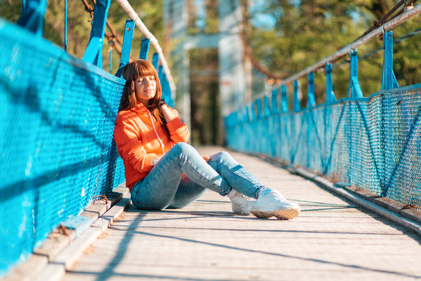 Sommerzeit. Eine junge Frau sitzt mit geschlossenen Augen in der Mitte der Brücke und sonnt sich in der Sonne. Draußen. - Foto, Bild