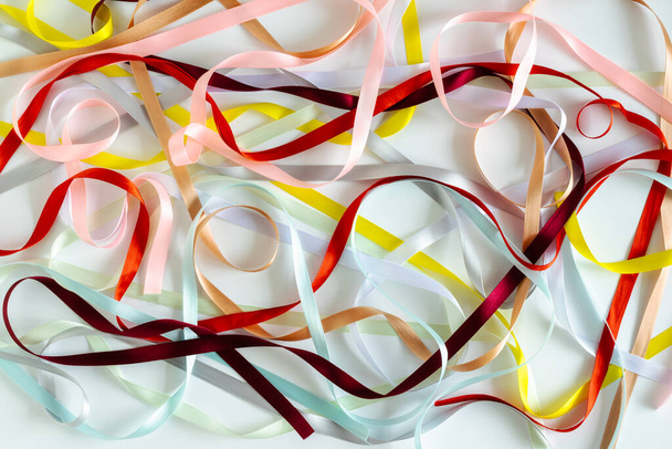 Multicolored narrow satin ribbons spread out in a chaotic manner on a white background. Abstract rainbow background. Horizontal photo.  - Photo, Image