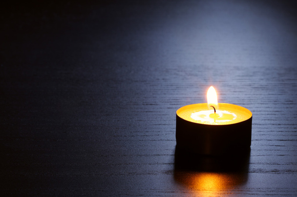 暗い木製のテーブルの単一の蝋燭は背面に点灯します。セレクティブ フォーカスでのショットを閉じる. - 写真・画像