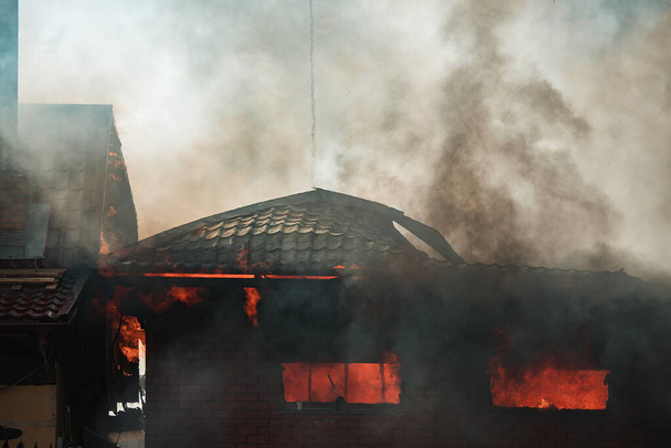 Огонь разрушает здание. Пожарные поливают водой горящий дом. Люди задыхаются от дыма и смога от огня. пожарные - Фото, изображение