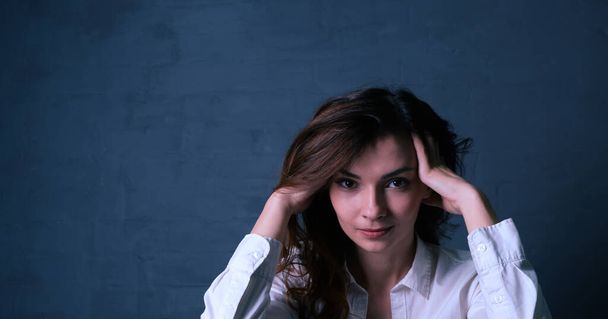 Portrait of a young brunette woman holding her head against a gray brick wall background - Photo, Image