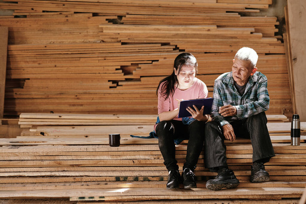 Дід і онука відпочивають на дерев'яних дошках і працюють над ескізом проекту для клієнта
 - Фото, зображення