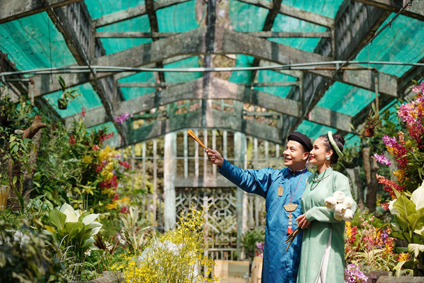 Happy young Vietnamese man showing beautiful flowers in greenhouse to bride - Photo, Image