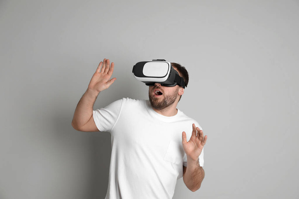 Emotional man using virtual reality headset on light grey background - 写真・画像