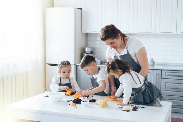 A mãe com três crianças faz biscoitos com doces. Atividade de lazer com conceito de crianças - Foto, Imagem
