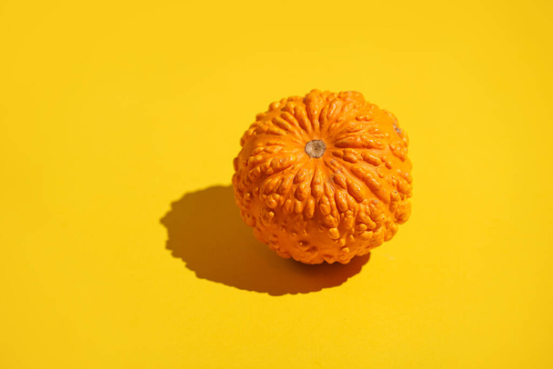 Pieni oranssi kurpitsa kirkkaan keltaisella pinnalla - Valokuva, kuva
