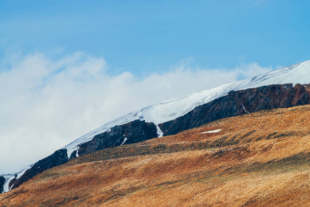 Огромные живые каменистые холмы и скалы со снегом при солнечном свете. Красочный солнечный высокогорный пейзаж с красной горой под голубым небом. Прекрасный альпийский пейзаж с холмом в красно-оранжевых коричневых тонах. - Фото, изображение