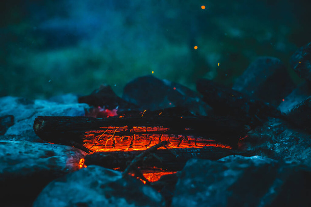 火の近くで焼かれた鮮やかな色付きの薪。キャンプファイアと青煙のオレンジの炎と大気暖かい背景。たき火の素晴らしいフルフレームイメージ。美しい火災でログを燃焼. - 写真・画像