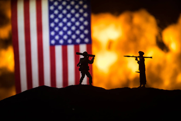 Amerikaanse vlag op brandende donkere achtergrond. Concept van oorlogscrisis en politieke conflicten tussen naties. Silhouet van een gewapende soldaat tegen een vlag van de VS. Selectieve focus - Foto, afbeelding