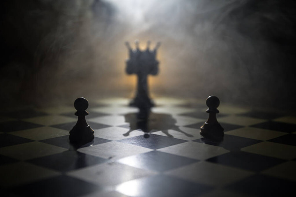 Beautiful crown miniature on chessboard. chess board game concept of business ideas and competition and strategy ideas concept. Chess figures on a dark background with smoke and fog. Selective focus - Photo, Image