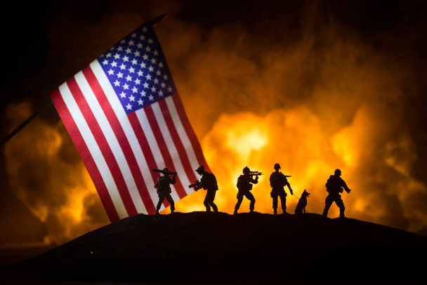 暗い背景に燃える上で米国の小さな旗。戦争の危機と国家間の政治的紛争の概念。アメリカの旗に対する武装した兵士のシルエット。選択的焦点 - 写真・画像