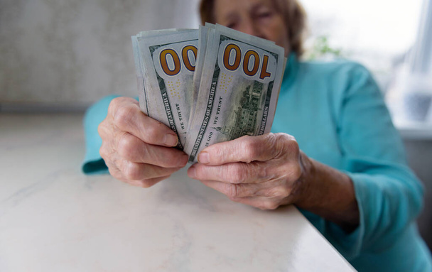 Κοντινό πλάνο των χεριών μιας ηλικιωμένης γυναίκας που κρατάει χρήματα σε χαρτονομίσματα των 100 δολαρίων, αποζημίωση. - Φωτογραφία, εικόνα