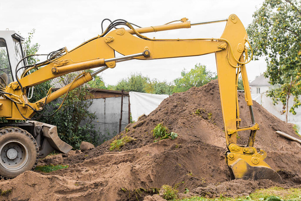 Egy hidraulikus dugattyú és egy vödör kotró ássa a földet egy halom homok mellett egy ipari területen.. - Fotó, kép