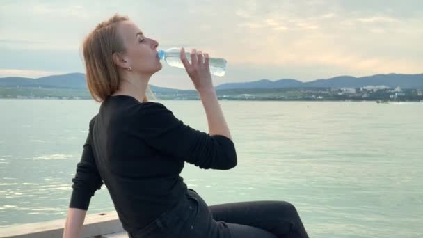 Žena pitná voda z láhve na mořském pobřeží - Záběry, video