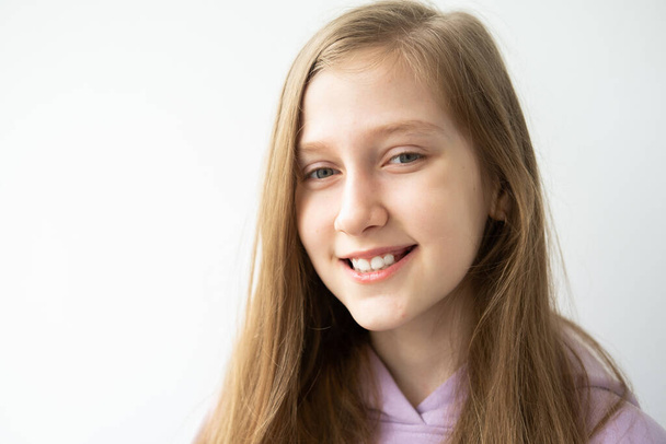 portrét krásné dospívající dívky s dlouhými vlasy ve fialové huddy stojící proti bílé zdi. - Fotografie, Obrázek