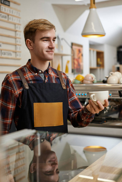 male waiter in apron holding cup of hot drink - 写真・画像