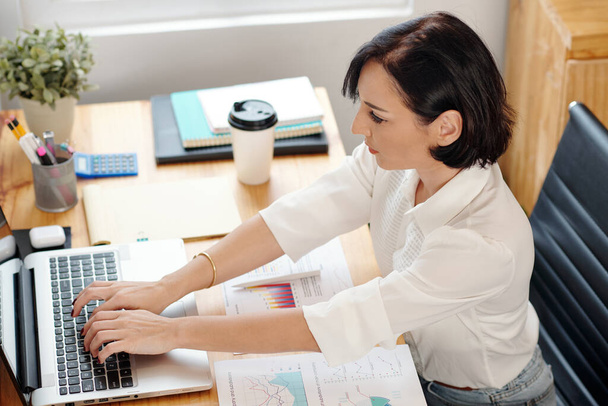 Jeune femme d'affaires travaillant avec des documents financiers et remplissant le formulaire sur ordinateur portable faire rapport - Photo, image