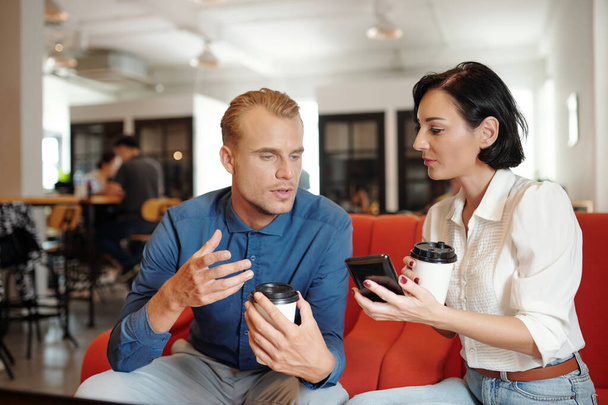 Νέοι επιχειρηματίες που πίνουν καφέ σε cafe και επιλέγουν νέα εφαρμογή για κινητά τηλέφωνα για διαχείριση έργων - Φωτογραφία, εικόνα