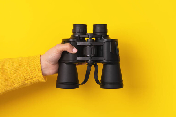 hand holding binoculars over yellow background - 写真・画像