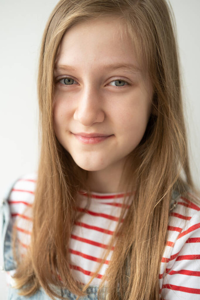 portrait de belle adolescente aux cheveux longs souriant debout contre un mur blanc. - Photo, image