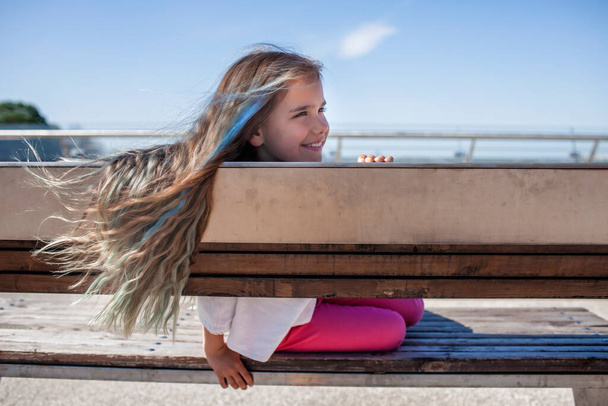 Morena menina pré-adolescente com destaques de cor azul olhando para o rio na ponte, vista lateral, dia de verão - Foto, Imagem