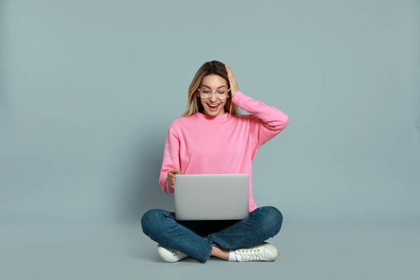 Young woman with modern laptop on grey background - Foto, imagen
