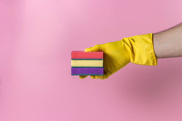 Hand holds a sponge for washing on a pink background. Cleaning tools on a colored background. Indoor cleaning tools. - 写真・画像