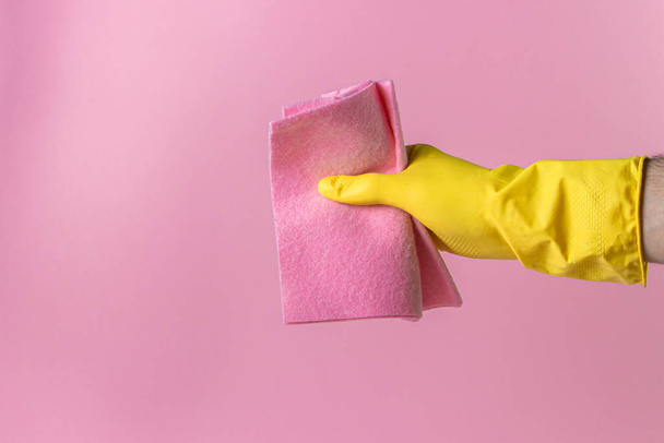 A mão segura um trapo de limpeza em um fundo rosa. Ferramentas de limpeza em um fundo colorido. Ferramentas de limpeza interior. - Foto, Imagem